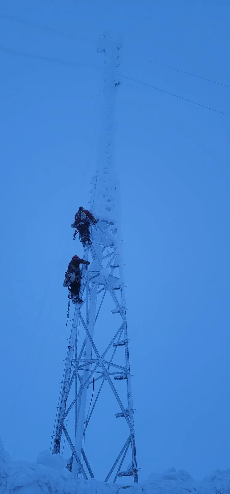 Two climbers ascending an ice-coated lattice tower